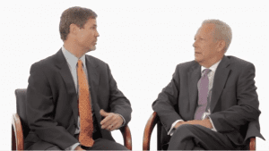 Two men in suits sitting next to each other.